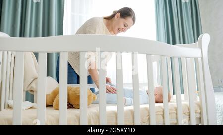 SMiling young mother with her little baby son lying in cradle at morning. Concept of parenting, family happiness and baby development. Stock Photo
