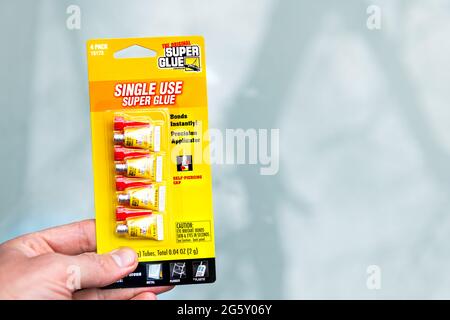 Nellysford, USA - April 29, 2021: Hand holding packaged storebought super glue tubes in dollar store with sign label for single use Stock Photo