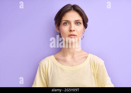 confident short haired woman looking seriously, isolated portrait on purple background. demure female in casual t-shirt having piercing gaze Stock Photo