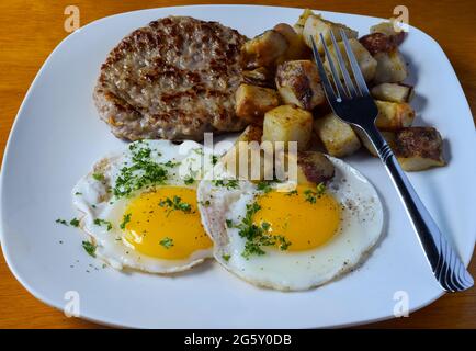 fried eggs top with parsley and served with sausage patty and home fries, Stock Photo