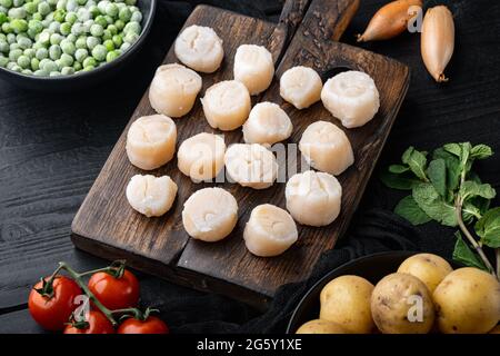 Fresh seafood scallops with herbs and vegetables, on black wooden background Stock Photo