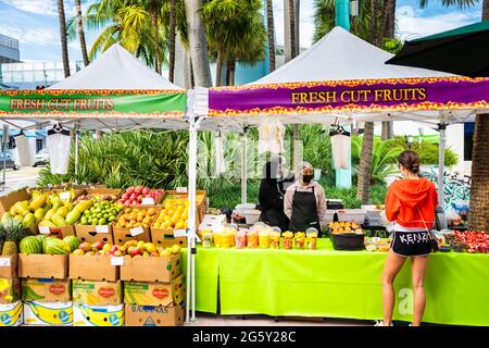 Miami Beach, USA - January 17, 2021: Famous Lincoln road shopping street with produce vegetable fruit stand stall outside at farmers market and people Stock Photo