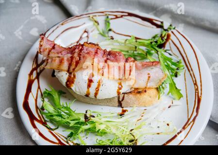 Delicious light breakfast poached egg on bruschetta with bacon, frisee salad and balsamic sauce dressing. Stock Photo