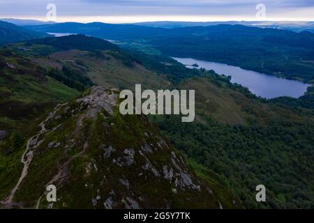 Ben Aa'n, Loch. Lomonnd and Trossachs National Park, Scotland, UK. 30th June, 2021. PICTURED: Walkers which resemble the size of ants in this drone photograph on the summit of Ben A'an enjoy the breath taking view of the surrounding lochs of Loch Katrine and Loch Achray and the surrounding peaks of the Trossachs area during an overcast evening. Credit: Colin Fisher/Alamy Live News Stock Photo