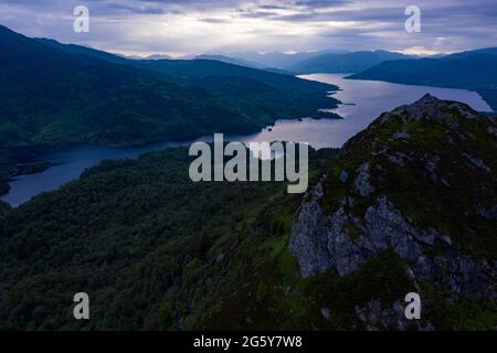 Ben Aa'n, Loch. Lomonnd and Trossachs National Park, Scotland, UK. 30th June, 2021. PICTURED: Walkers which resemble the size of ants in this drone photograph on the summit of Ben A'an enjoy the breath taking view of the surrounding lochs of Loch Katrine and Loch Achray and the surrounding peaks of the Trossachs area during an overcast evening. Credit: Colin Fisher/Alamy Live News Stock Photo