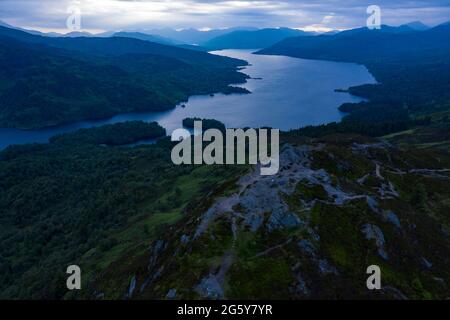 Ben Aa'n, Loch. Lomonnd and Trossachs National Park, Scotland, UK. 30th June, 2021. PICTURED: Walkers which resemble the size of ants in this drone photograph on the summit of Ben A'an enjoy the breath taking view of the surrounding lochs of Loch Katrine and Loch Achray and the surrounding peaks of the Trossachs area during an overcast evening. Credit: Colin Fisher/Alamy Live News Stock Photo