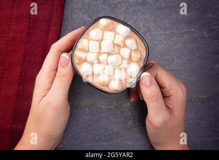 A Woman Holding a Cup of Hot Chocolate with Marshmallows on a Dark Table Stock Photo