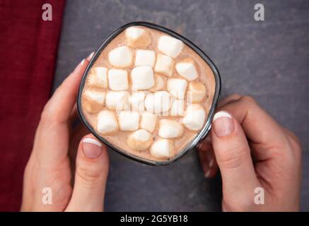 A Woman Holding a Cup of Hot Chocolate with Marshmallows on a Dark Table Stock Photo