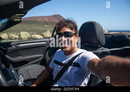 Smiling Indian man sitting in his convertible car takes a selfie, he is smiling and happy, wearing sunglasses. Successful man Stock Photo