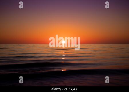 Distant Sun setting in clear skies over a calm and serene ocean of perfection Stock Photo