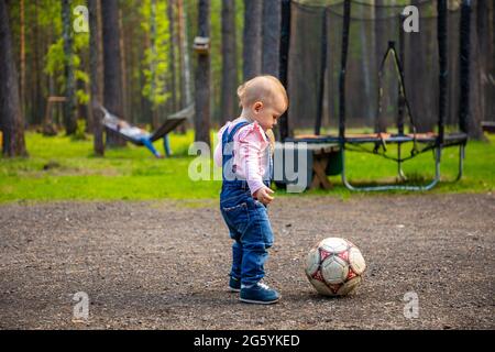 little active girl baby blond playing with football ball in the forest, Russia Stock Photo