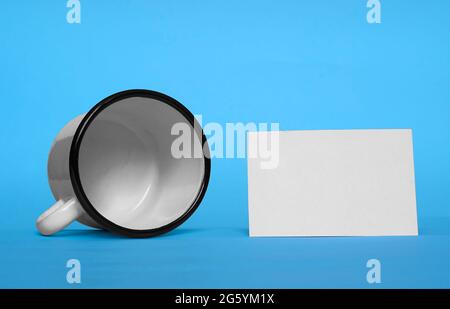 White metal cup is lying on its side and white paper card Stock Photo
