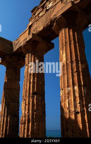 Patches of original stucco or plaster stand out against pitted stonework in bright Mediterranean sunshine warming fluted Doric columns of the reconstructed colonnade of the Temple of Hera or Temple E in the ruins of the ancient Greek city and port of Selinus or Selinous at Selinunte in southwest Sicily, Italy.  Although the temple probably collapsed in earthquakes after Selinus was abandoned, it was reconstructed in 1958 using the original materials. Stock Photo