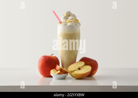 Apple milkshake with cream decorated with fruit around on white wooden table and light isolated background. Front view. Stock Photo