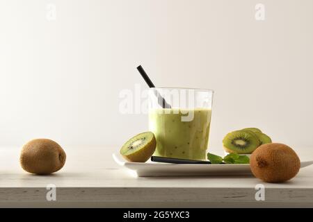 Kiwi drink glass presentation on plate with cut fruit on wooden table with isolated background. Front view. Stock Photo
