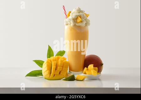 Mango milkshake with cream decorated with fruit around on white wooden table and light isolated background. Front view. Stock Photo