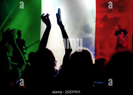 football fans supporting Italy - crowd celebrating in stadium with raised hands against Italy flag Stock Photo