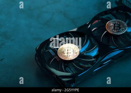 Gold bitcoin coins lie on the cooler of a powerful video card with cyanide neon illumination. Stock Photo