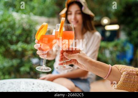 Women in terrace clinking with orange fruit cocktails. Closeup on the hands holding glasses. Blurred people. Stock Photo