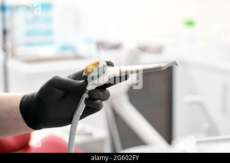 The gloved hand of the dentist holds the Airflow whitening and cleaning brush to remove tartar and plaque. Stock Photo