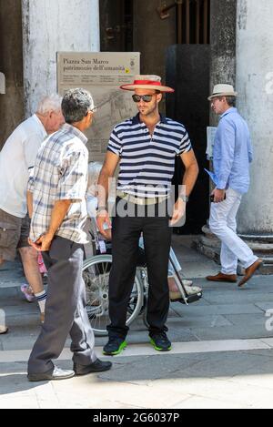 A gondolier wearing his traditional blue & white striped shirt and boater with a red headband, touting for business in Venice, northern Italy Stock Photo