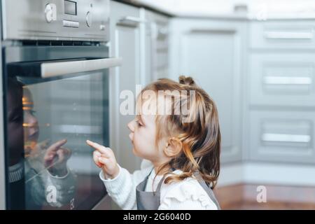 Little girl looking at oven, waiting prepare of food. Stock Photo