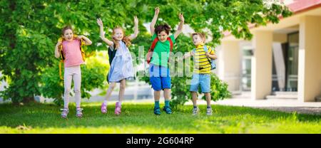Cute children with rucksacks jumping and playing in the park near the school Stock Photo