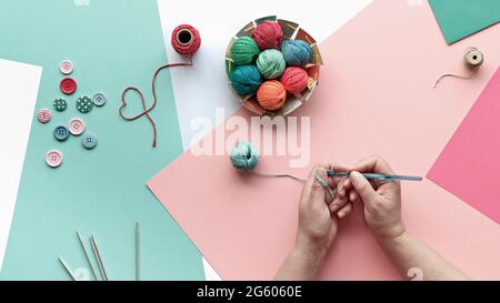 Cotton yarn balls, hands with crochet. Creative knitting hobby. Panoramic background in pink, mint green, white. Creative arrangement on layered pink Stock Photo