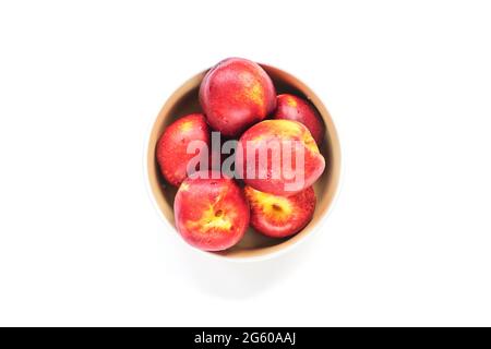 Ripe red peaches in a bowl isolated on white. Top view, flat lay. Stock Photo