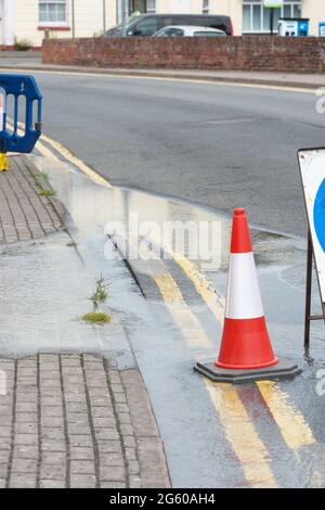 Water flows from a burst water main pipe under a road - note the bulging road surface June 2021 UK Stock Photo