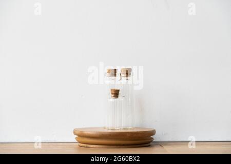 Three glass bottles with cork stopper on wooden podium with white wall background. Essential oil refilling store. Mockup template.  Stock Photo