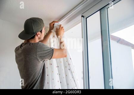 Young man installing curtains over window at home Stock Photo