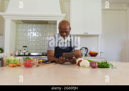 Senior african american man cooking in kitchen using tablet Stock Photo