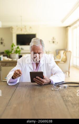Senior caucasian male doctor sitting at table using tablet computer Stock Photo