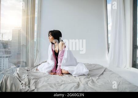 young armenian woman looking through window in bedroom Stock Photo