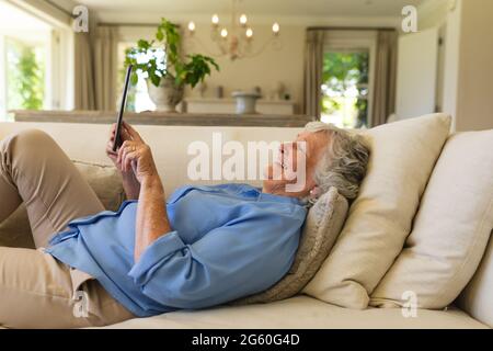 Senior caucasian woman lying on sofa using tablet Stock Photo