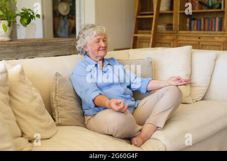 Senior caucasian woman sitting on sofa meditating with eyes closed Stock Photo