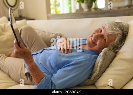 Portrait of senior caucasian woman lying on sofa using tablet Stock Photo
