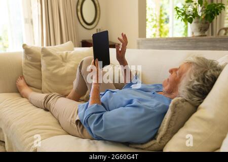 Senior caucasian woman lying on sofa using tablet Stock Photo