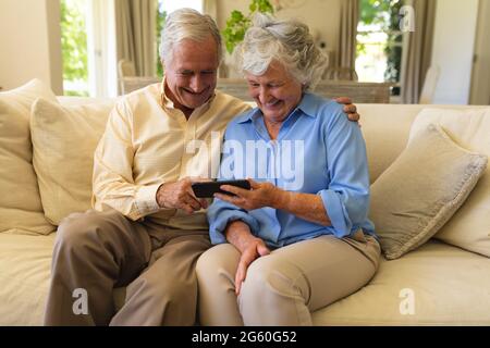 Senior caucasian couple sitting on sofa using smartphone and smiling Stock Photo