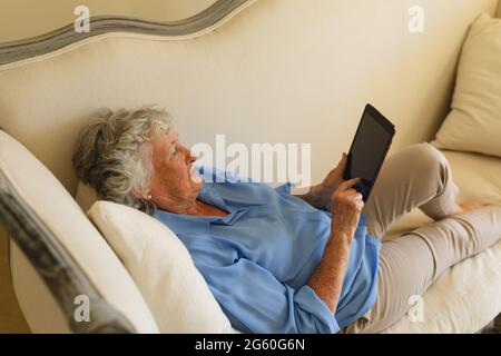 Senior caucasian woman lying on sofa and using tablet Stock Photo