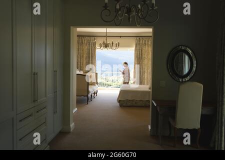 Senior caucasian woman standing next to window using smartphone in bedroom Stock Photo