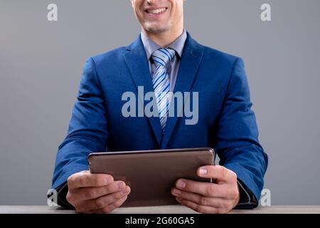 Smiling caucasian businessman using tablet, isolated on grey background Stock Photo