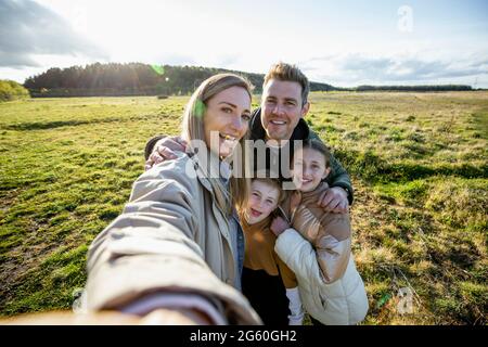 A front-view shot of a caucasian mother and father with their son and daughter, they're all taking a break from walking by smiling for a selfie with a Stock Photo