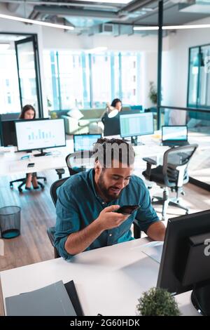 Mixed race businessman sitting at table using smartphone with colleagues in background Stock Photo