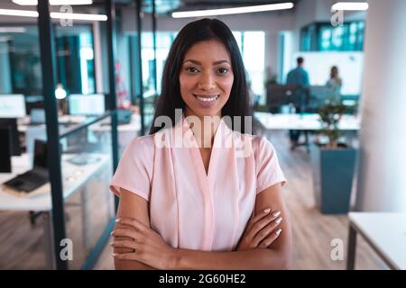 Portrait of mixed race businesswoman smiling with arms crossed with colleagues in background Stock Photo