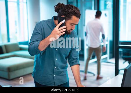 Mixed race businessman using smartphone with colleagues working in background Stock Photo