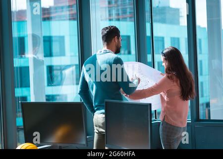 Two diverse businesspeople discussing together and holding scheme at window Stock Photo