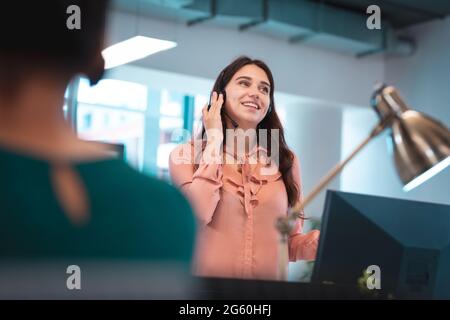 Caucasian businesswoman wearing headset and sitting at table talking, using computer Stock Photo