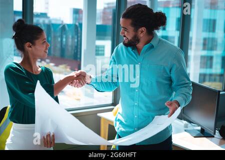 Two diverse businesspeople shaking hands discussing together and holding scheme Stock Photo